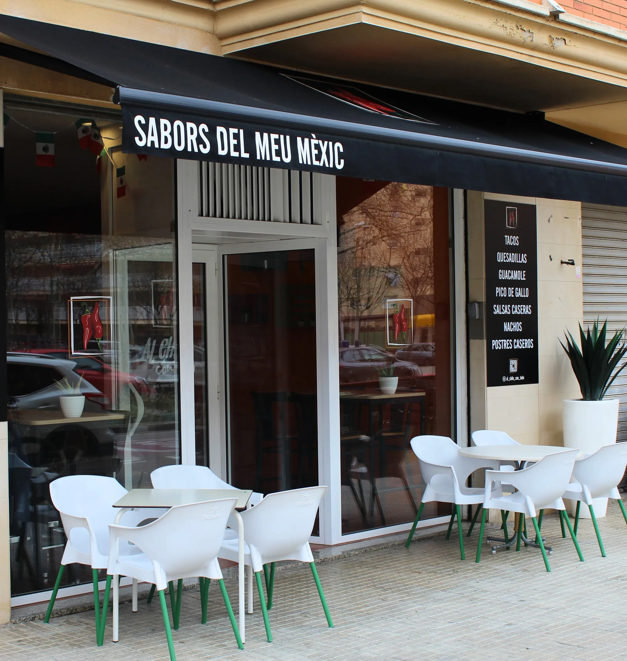 La fachada con el toldo negro «Sabors del meu Mèxic» y la terraza de sillas blancas